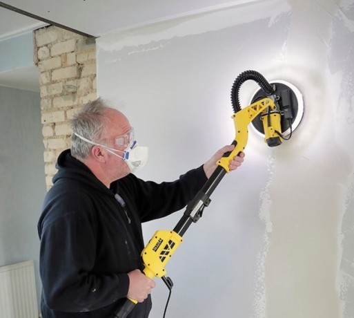 Mężczyzna szlifujący ściany w stroju ochronnym szlifierką Stanley FATMAX SFMEE500S-QS